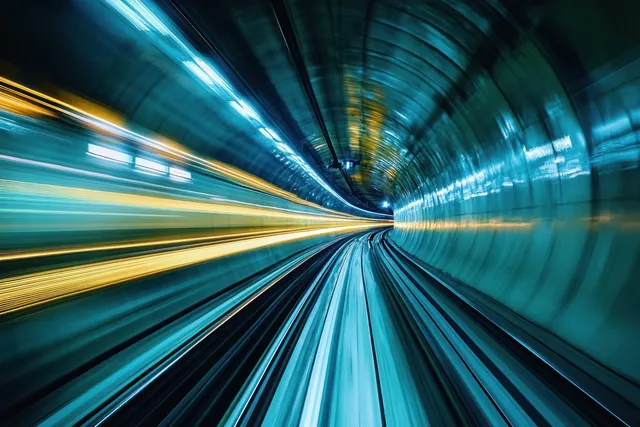 Blue and yellow light trails blur through a curved underground tunnel interior with rail motion.