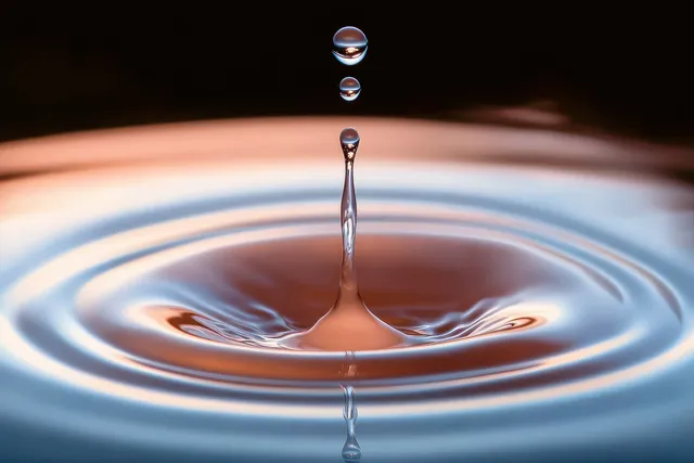 A macro water droplet splashes into a reflective surface, sending concentric ripples across the pool.