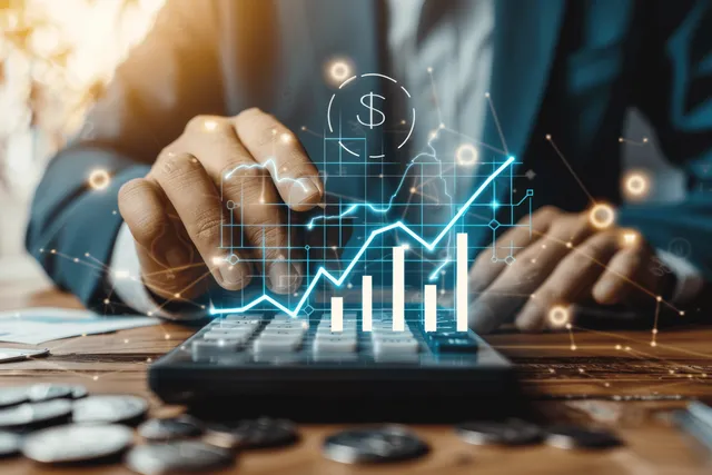 A hand grips a calculator on a desk while an upward financial chart and dollar symbol overlay appear on screen.