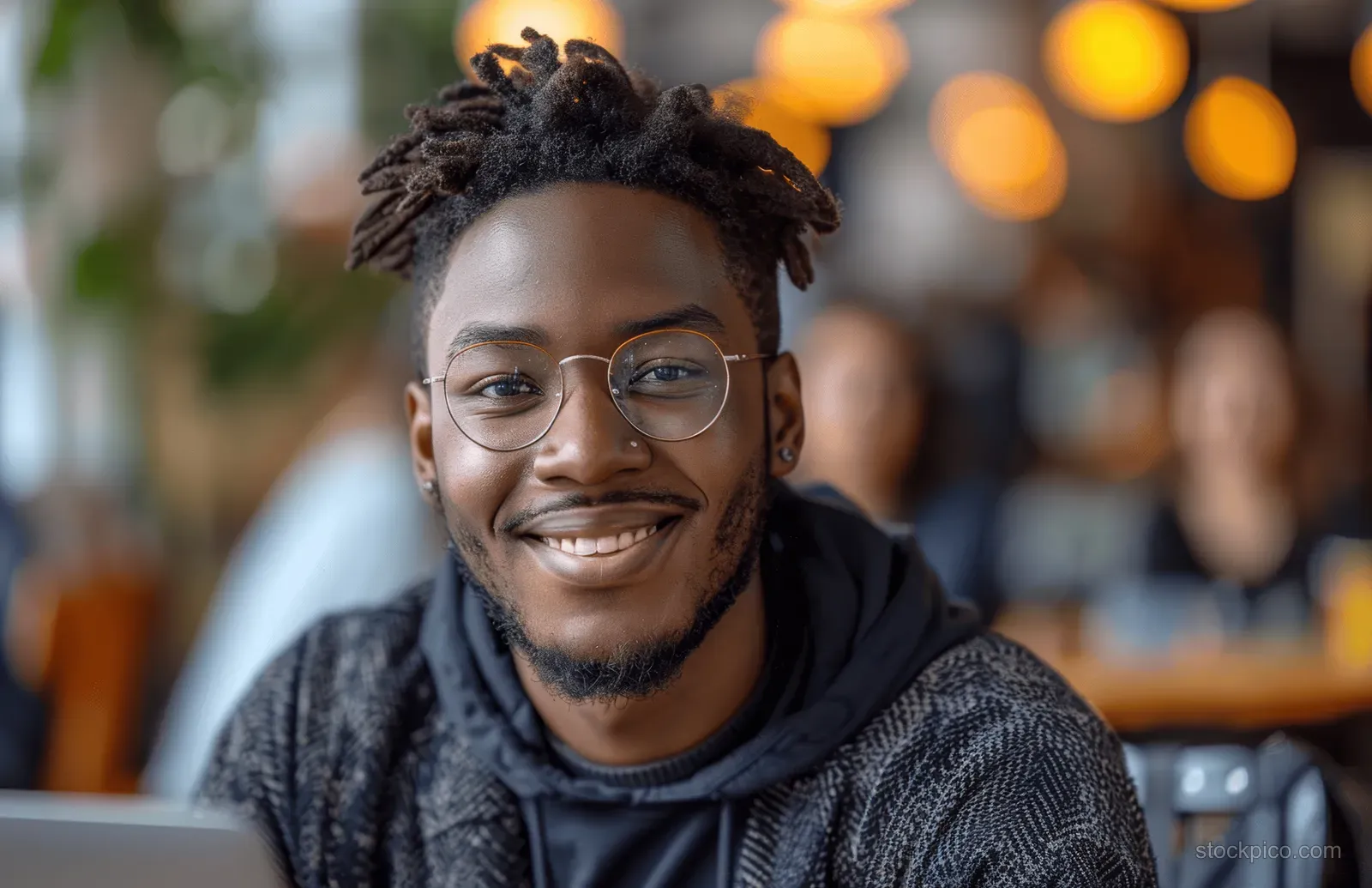 Smiling man with glasses seated at an office table while coworkers appear blurred behind him.