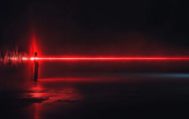 Silhouette facing a wall as a bright red laser beam stretches into misty darkness