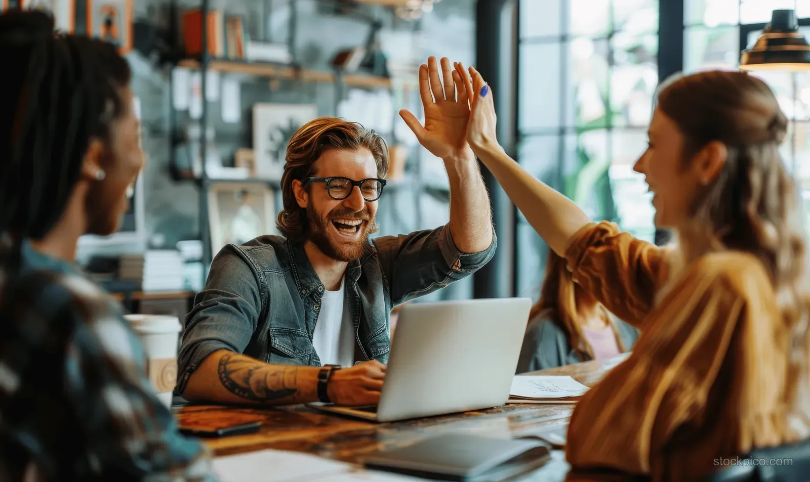 Coworkers at a conference table raise hands for a high five during a business meeting with laptops.
