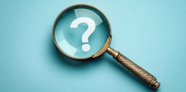 Antique magnifying glass over a white question mark on blue background with focused lens