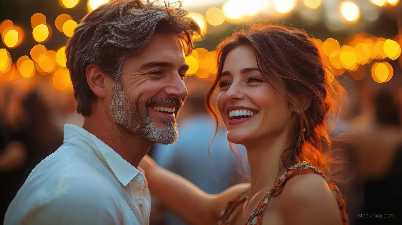Smiling couple laughing together outdoors at night with warm glowing bokeh lights behind them.