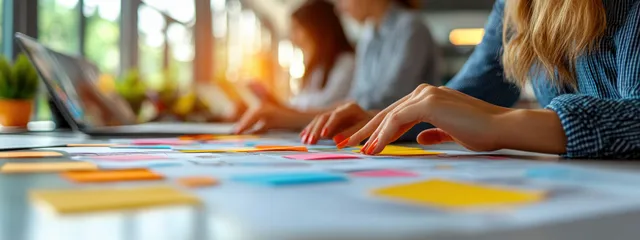People’s hands arrange colorful sticky notes on a busy office table during a collaborative planning meeting.