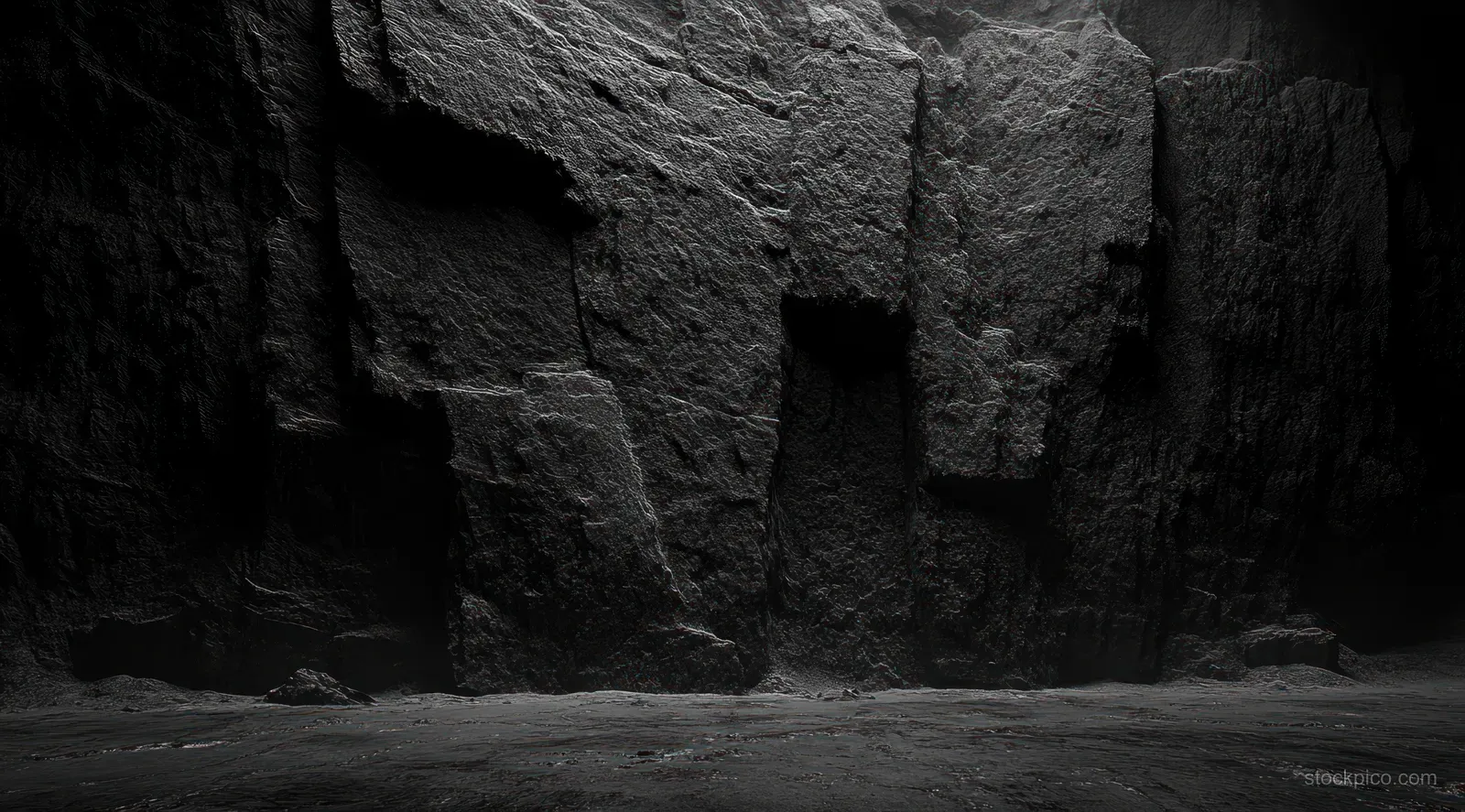 A dark rocky cliff wall with rough stone texture and softly lit cave shadows along an uneven floor.
