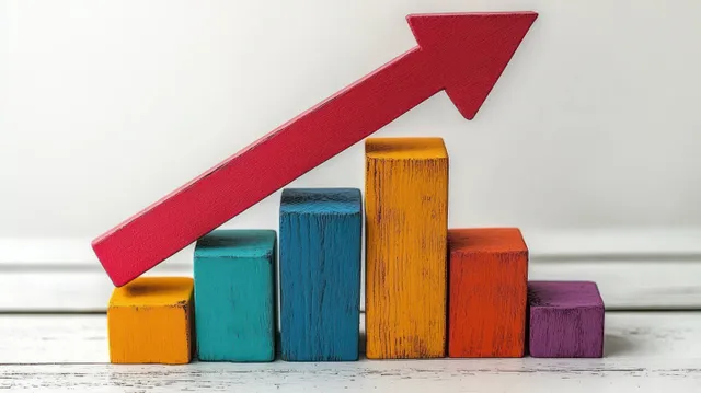 Colorful wooden blocks form a rising bar chart with a large red arrow pointing upward on a light background.