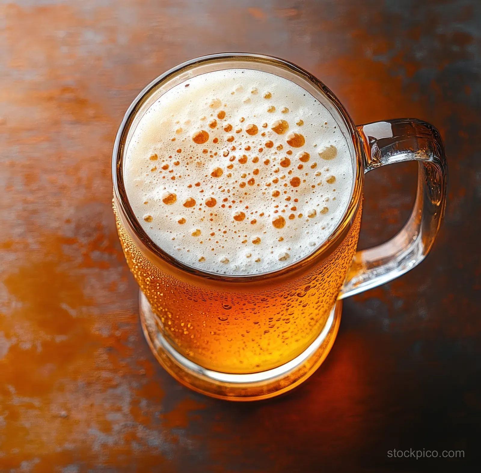 Amber beer with a frothy foam head in a cold glass mug, showing condensation on a dark textured table.