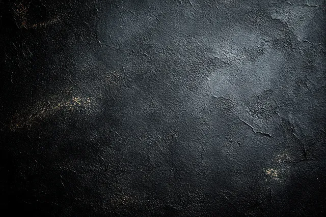 Close-up of a dark weathered concrete wall with cracks, pitted texture, and faint light patches.