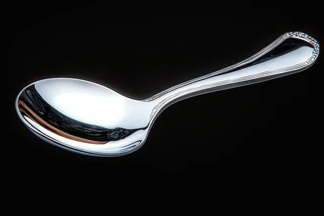 A polished silver spoon lies on a black background with bright reflections on its bowl and handle.