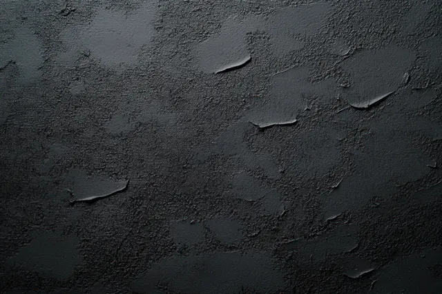 Close-up of a dark concrete wall with peeling paint and flaking weathered patches.