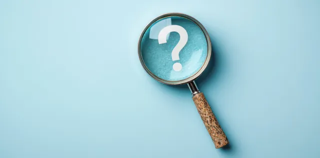 Magnifying glass with wooden handle enlarging a white question mark on a light blue background.