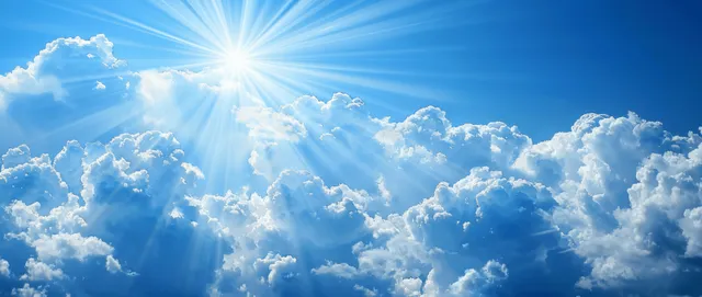 Sun rays burst through white clouds in a clear blue summer sky.