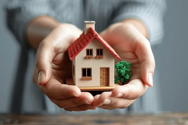 Hands holding a miniature house model with a small tree, symbolizing home insurance protection against risk.