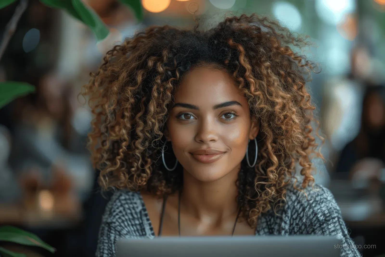 Curly-haired businesswoman typing on a laptop during a team meeting in a softly lit office.