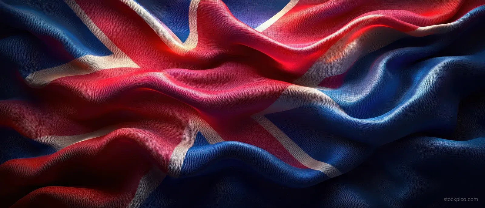 Union Jack flag waves in the wind with rippling textured fabric and dramatic highlights across blue, red, and white.