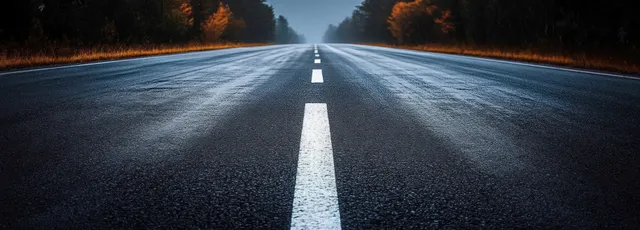 Wet twilight highway road stretches into the distance with bright white lane markings and dark reflective asphalt.