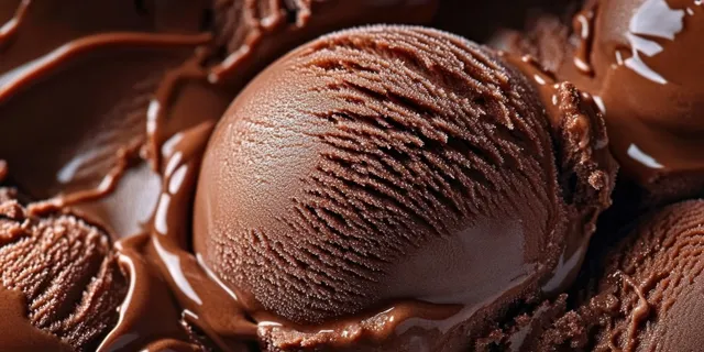 Chocolate ice cream scoops melt on a surface, showing glossy cocoa texture and frosty highlights.