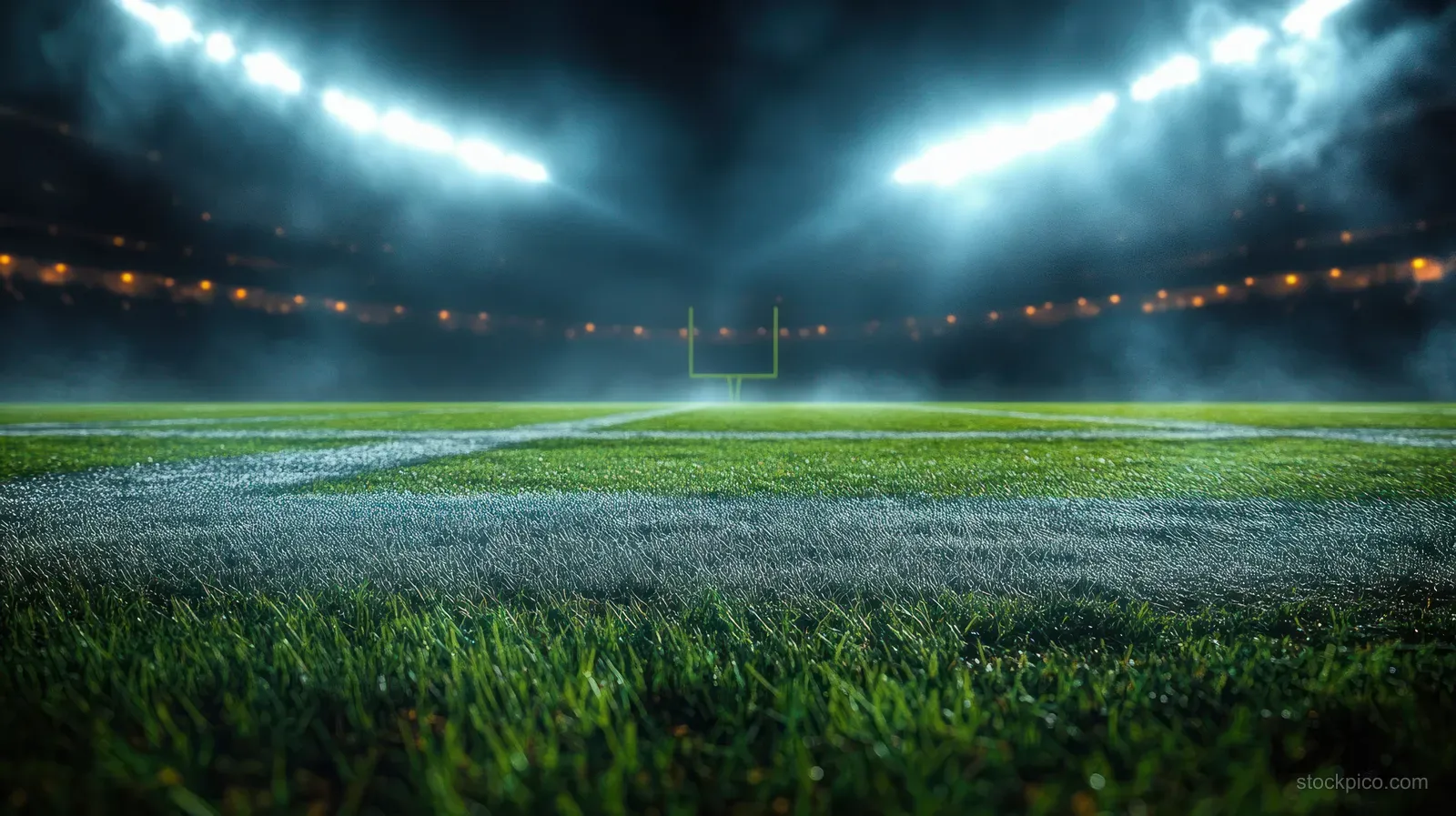 Football goal and yard lines on green turf beneath bright stadium lights at night.
