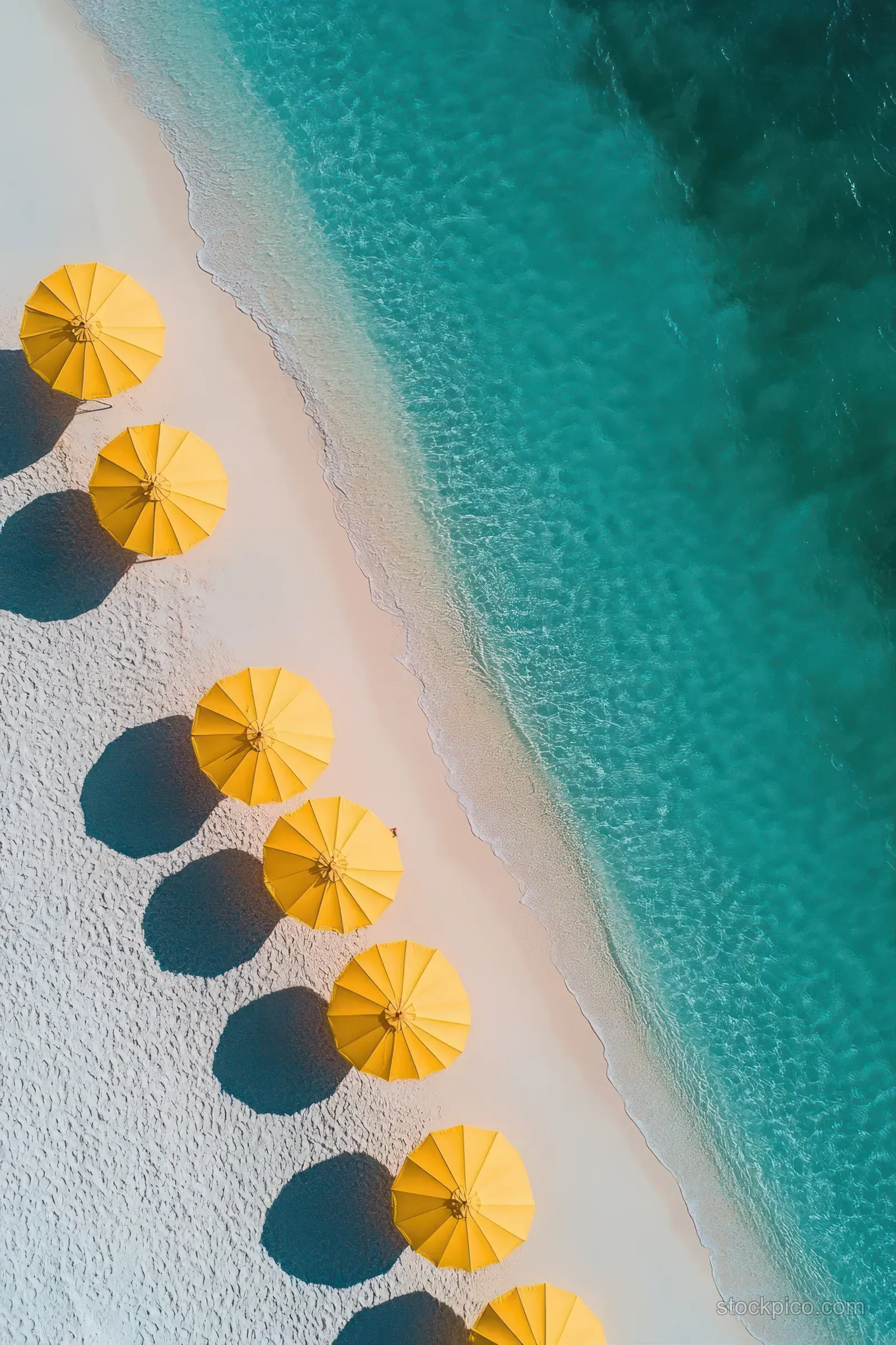 Aerial view shows yellow umbrellas on white sand with sharp shadows and turquoise water along the coast.