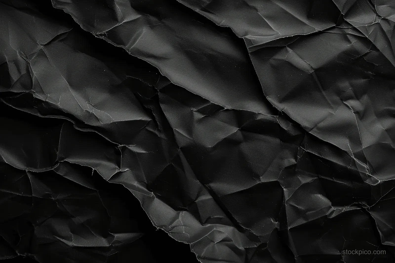 Dark black crumpled paper texture with deep creases and layered folds filling the frame.