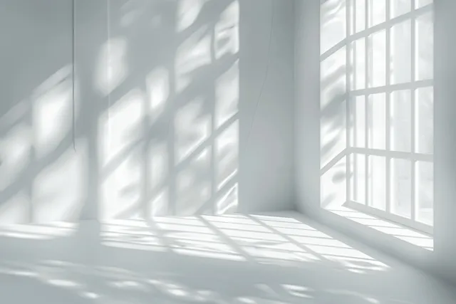 Sunlight and shadow grid patterns illuminate a white wall beside tall window panes.