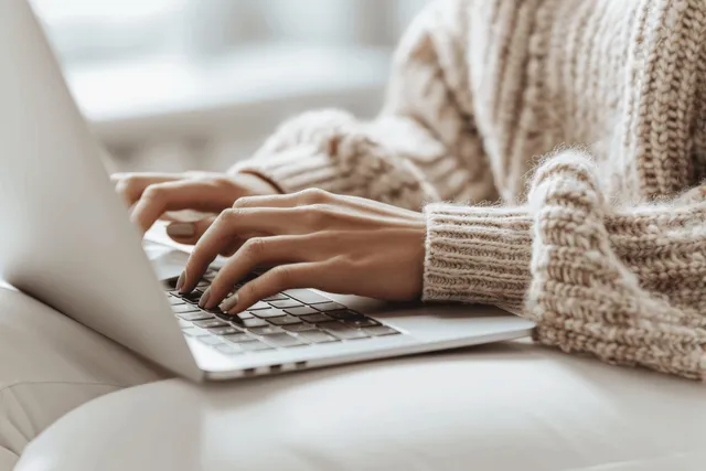 A woman’s hands typing on a laptop keyboard in a cozy home office setting.