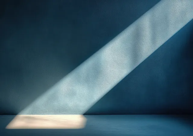 A daylight beam casts sharp geometric shadows across textured blue wall and floor.