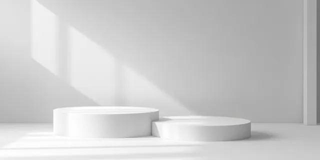 Two white cylindrical podiums in a bright studio, with daylight casting soft shadows on the wall.