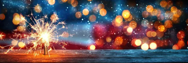 Handheld sparkler and American flag with warm bokeh lights against a rustic wooden background.