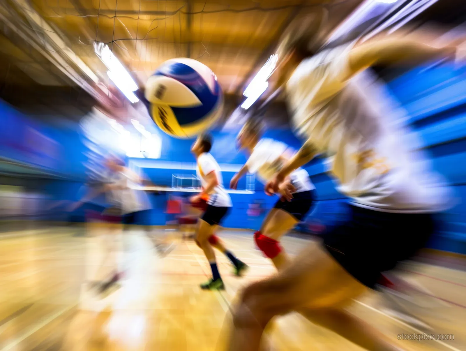 Motion-blurred indoor volleyball match shows a male player spiking with the ball arcing above the net.