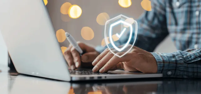 Hand typing on laptop with digital shield encryption overlay for data security