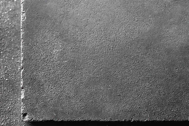 Close-up of a rough dark gray concrete wall edge with gritty texture in monochrome lighting.