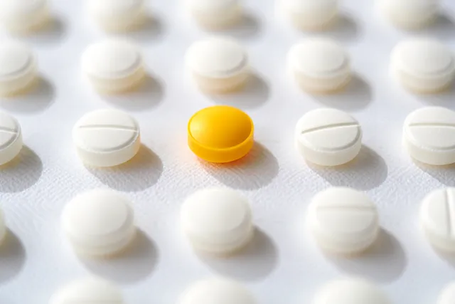 Bright yellow pill standing out among white tablets on a clean surface
