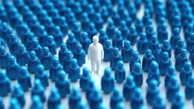 A lone white figurine stands among many small blue figurines arranged in rows.