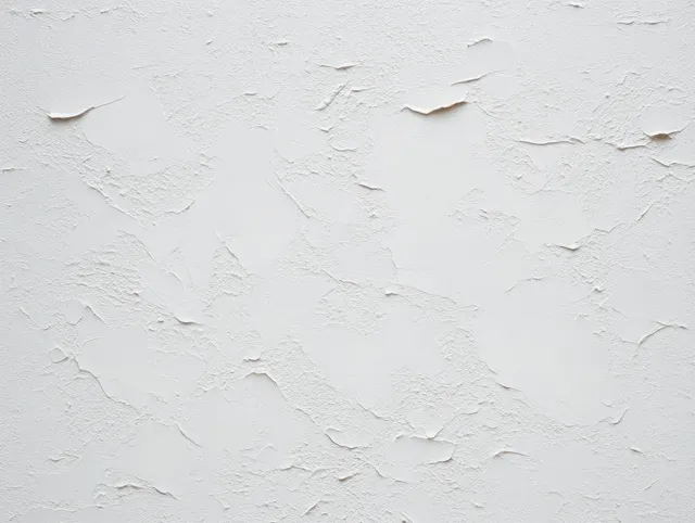 Close-up of a white wall with uneven plaster texture and peeling paint exposing rough patches.