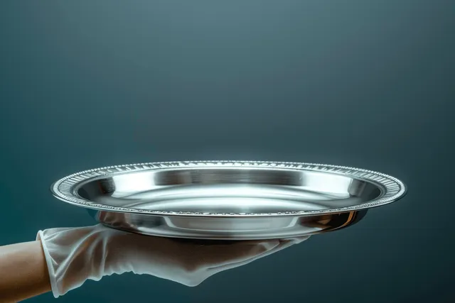 A gloved hand holds an empty silver tray against a muted grey background.