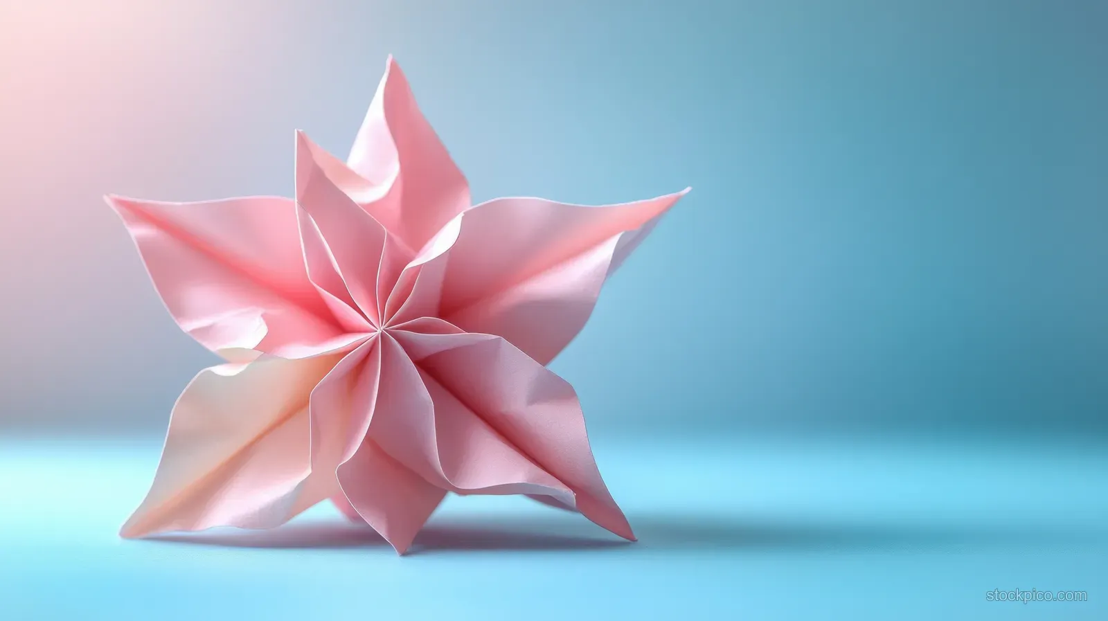 A soft pink folded star sculpture rests on a smooth light blue background with subtle shadows.