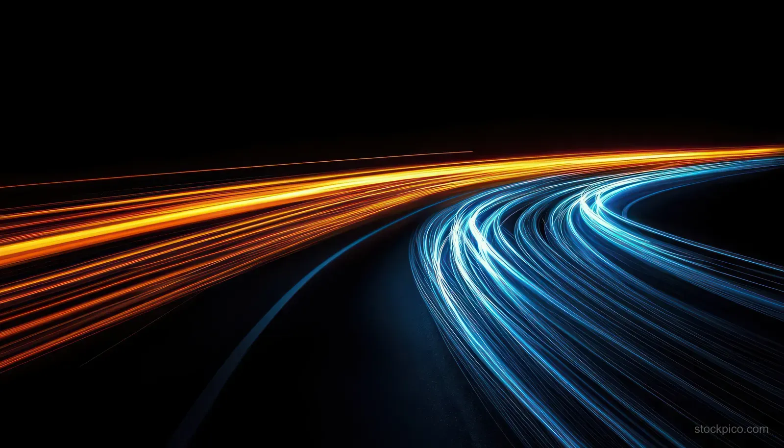 Long-exposure light trails in gold and blue sweep along a dark curving highway at night.