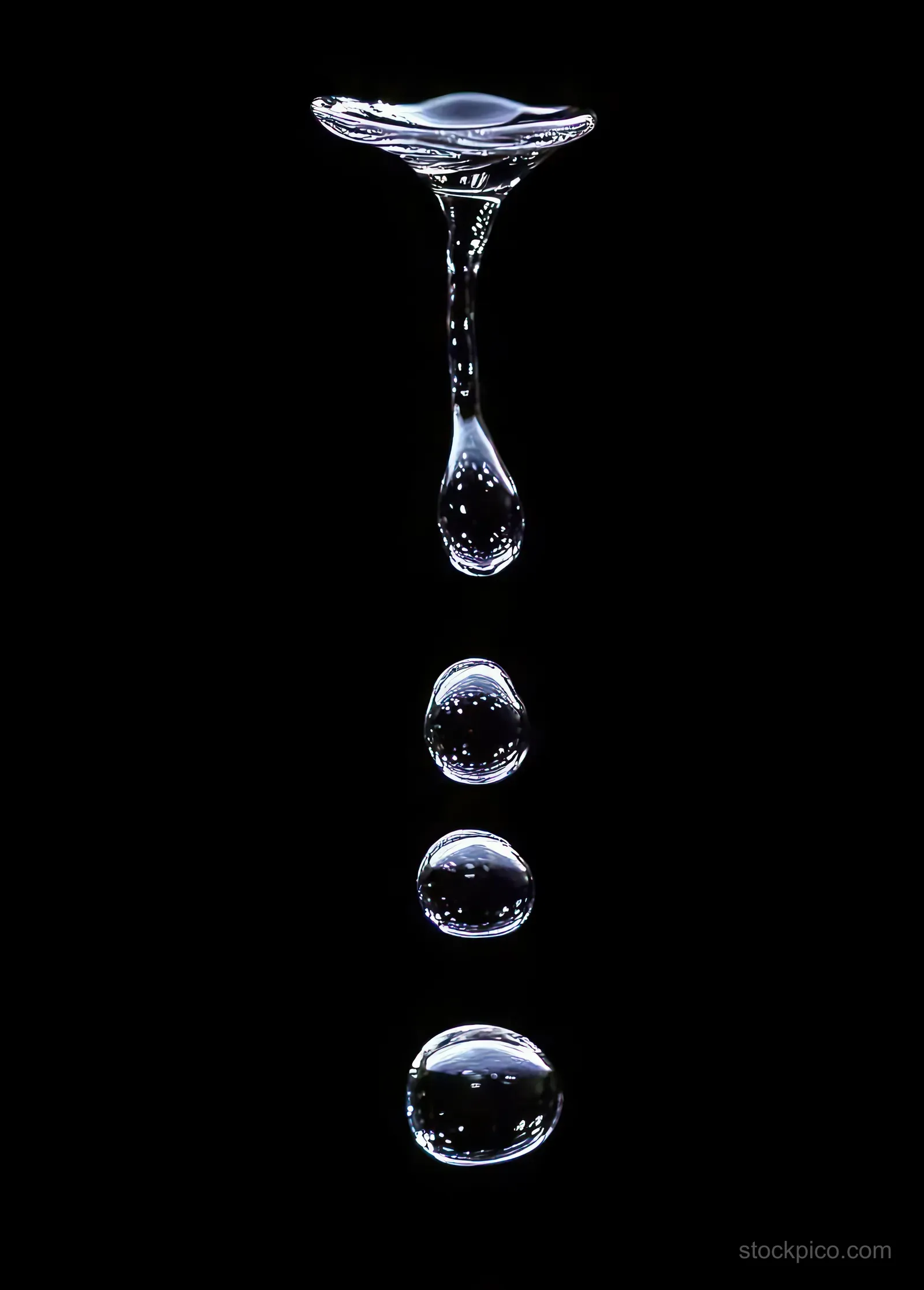 Multiple clear water droplets suspended in midair above a black background, showing crisp reflections and separation.