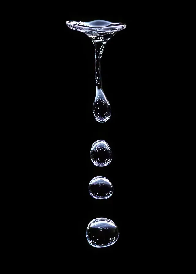 Multiple clear water droplets suspended in midair above a black background, showing crisp reflections and separation.