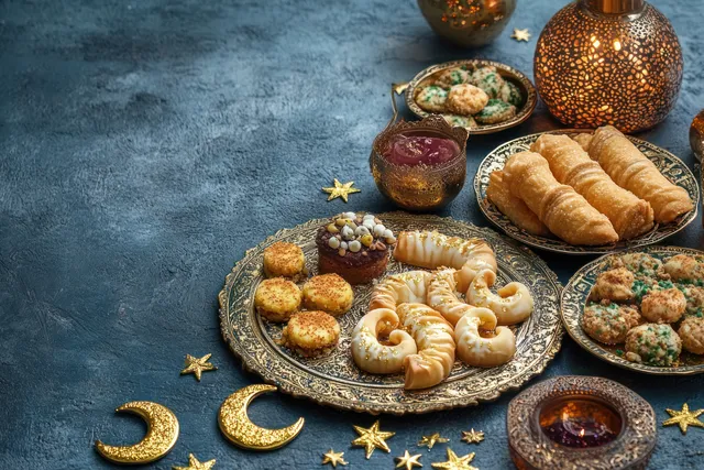Ramadan desserts and lanterns arranged on a blue textured surface with crescent decorations.