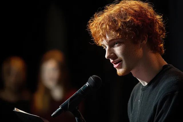 Red-haired young man speaking into microphone on dim stage
