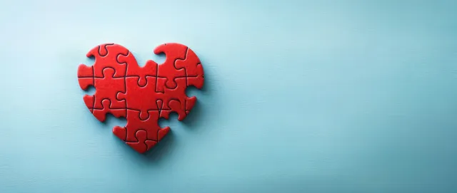 Red heart puzzle pieces arranged on a light blue background suggesting charity and care.