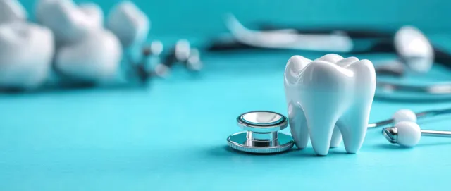 A white tooth model with a stethoscope and small dental tools on a blue surface in soft natural light.