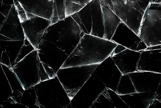 Jagged transparent glass shards with sharp reflective edges scattered on a dark background.