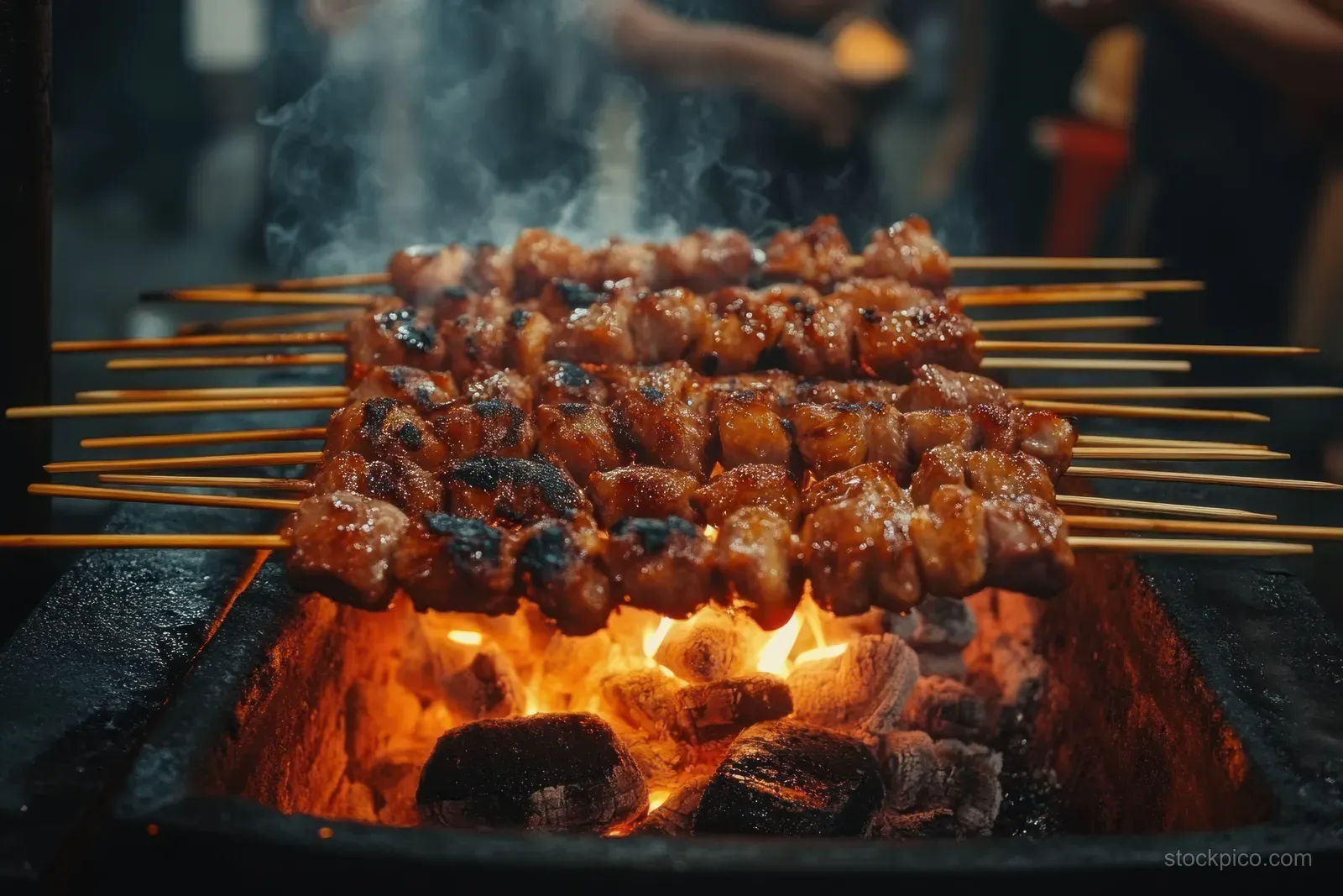 Chicken satay skewers grilling over hot charcoal with visible spice glaze and glowing flames.