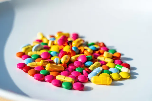 Close-up pile of colorful assorted pills and capsules scattered on a white surface with Dosage Forms