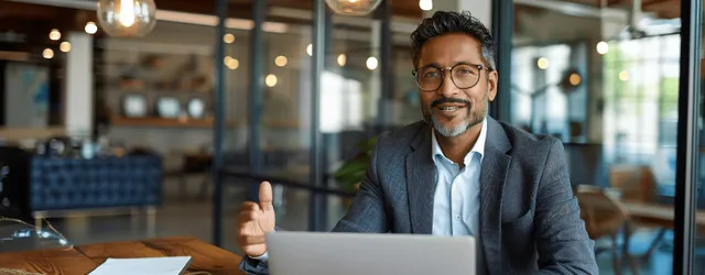 Indian businessman presenting on laptop in glass-walled office