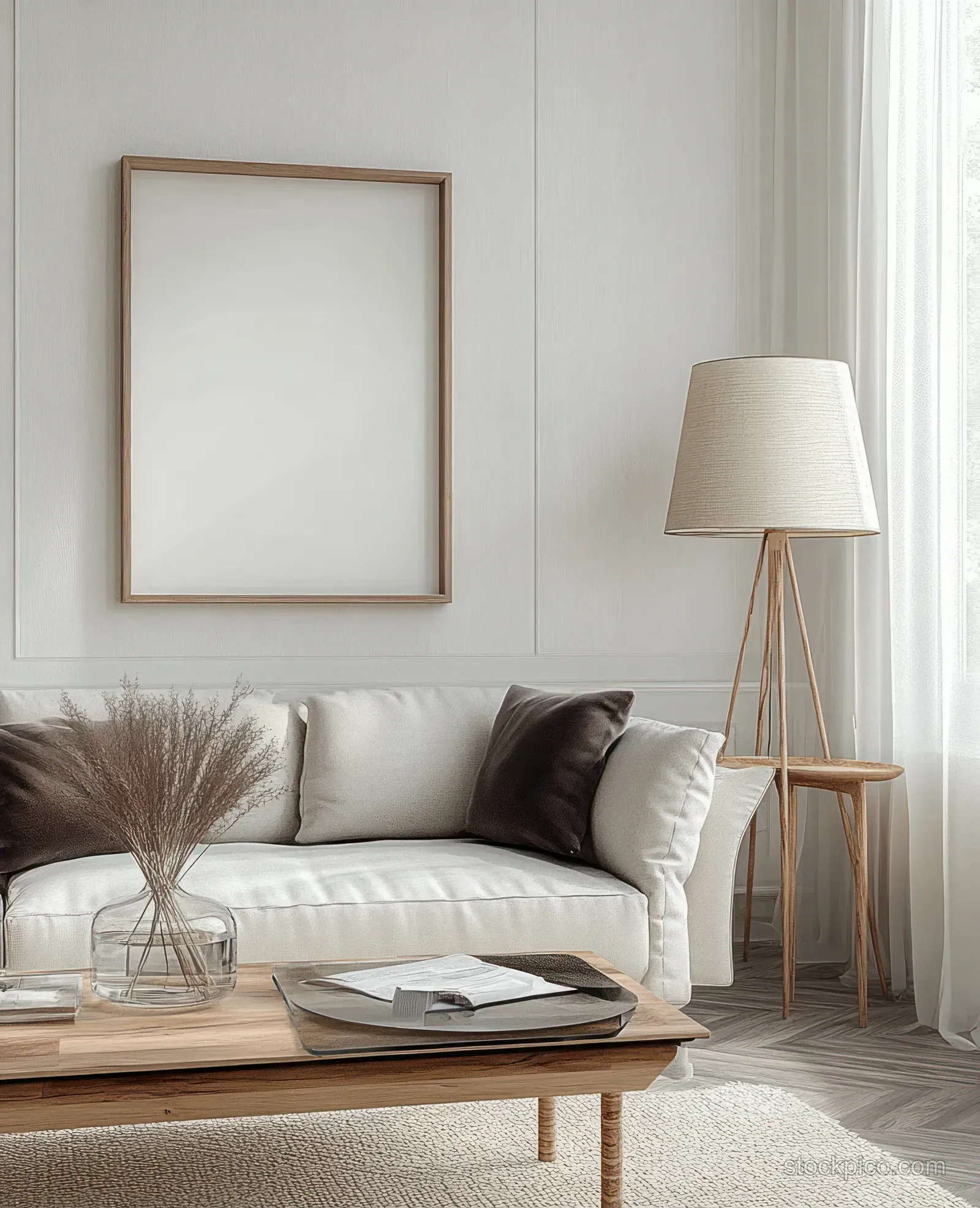 Minimalist living room with beige sofa, books on wooden coffee table, dried plants in a glass vase, and tripod floor lamp.